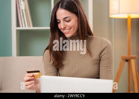 Giovane donna che fa acquisti online, ha una carta di credito e utilizza un computer portatile. Foto Stock
