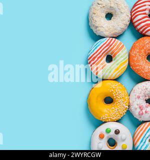Deliziose ciambelle smaltate su sfondo blu. Piatto quadrato Lay - Set di diverse donuts colorate o donuts su blu con spazio copia per il testo o il disegno. Luce solare brillante con ombre dure. Foto Stock