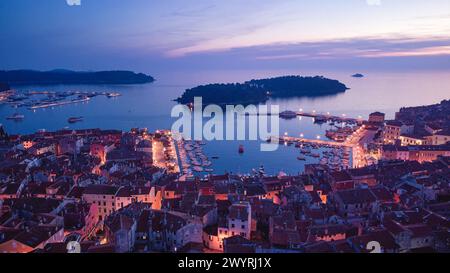 Vista panoramica della città serale al tramonto. Fotografia aerea. Luci sulle lanterne al crepuscolo. Le navi sono nella baia. Tetti piastrellati di case in t Foto Stock