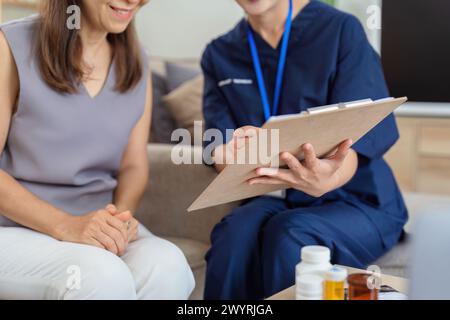 operatore sanitario che compila un modulo con una donna anziana durante una visita sanitaria domiciliare Foto Stock