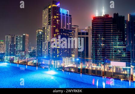 Splendida vista notturna sul tetto dei grattacieli della città di Kuala Lumpur, illuminata di notte, elegante piscina in primo piano con splendide viste panoramiche ad angolo alto Foto Stock