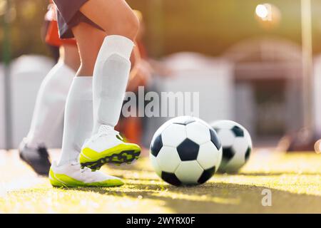 Pallone da calcio il giorno della domenica. Soccer Boy che corre con le scarpe bianche su Grass Pitch. Calcio sportivo con sfondo basso Foto Stock