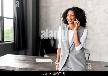 Immersa in una conversazione, la donna parla al telefono con un aspetto di ricerca mirata, in piedi in un moderno loft, una dipendente donna durante la conversazione sullo smartphone Foto Stock