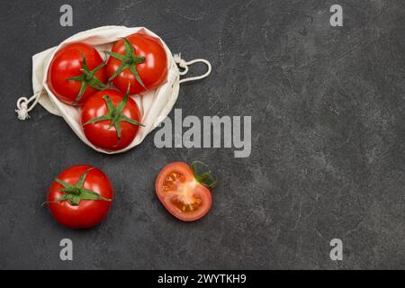 Pomodori in sacchetto a rete riutilizzabile. Pomodoro intero e spicchi di pomodoro tritato sul tavolo. Sfondo nero. Vista dall'alto. Copia spazio Foto Stock