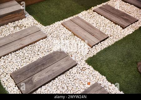 Un tranquillo giardino con gradini in legno che conducono a un sentiero di ghiaia circondato da vegetazione lussureggiante ed elementi decorativi Foto Stock