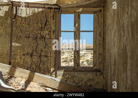 Un vecchio letto arrugginito si trova in posizione verticale accanto alla finestra della casa dei minatori di diamanti a Bogenfels, Namibia, da tempo abbandonata nel deserto. Foto Stock