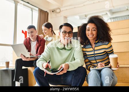 Un gruppo di studenti diversi, tra cui una ragazza nera, si siede insieme su un pavimento rustico in legno al coperto. Foto Stock