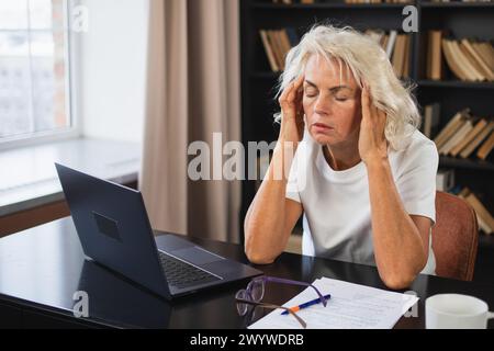 Mal di testa dolore. Donna di mezza età che tocca i templi e prova stress. Vecchia signora matura stanca del lavoro sentendo mal di testa malato sfregamento templi fronte. L Foto Stock