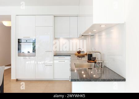 Interno di una nuova cucina ad angolo bianca. Potete vedere il lavandino e anche il forno. Spazio elegante con poche cose in vista. Piano di lavoro in marmo. Solo una teiera Foto Stock