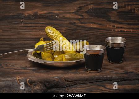 Tavola rustica in legno con sottaceti assortiti su piastra metallica e tazze di varie forme e dimensioni. Un picchetto visualizzato su una forchetta. Messa a fuoco selettiva con Foto Stock