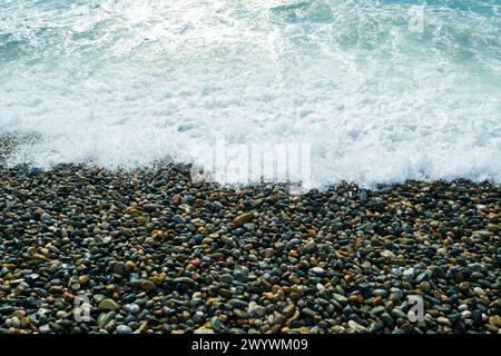 Ciottoli di mare e schiuma di mare. Costa rocciosa. Sfondi e texture naturali. Piccole pietre e un'onda sulla riva del mare. Foto Stock