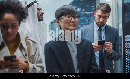 Quattro diverse persone multietniche viaggiano su un ascensore di vetro per raggiungere l'ufficio in un moderno centro affari. Arab Investor, Black Latin American Manager, Japanese Specialist e Caucasico businessman in a Lift. Foto Stock