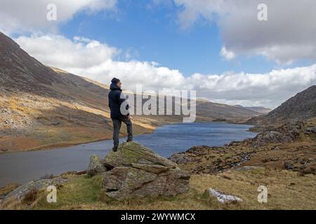 Uomo in piedi sulla roccia che si affaccia sul lago Llyn Ogwen, Snowdonia National Park vicino a Pont Pen-y-benglog, Bethesda, Bangor, Galles, Gran Bretagna Foto Stock