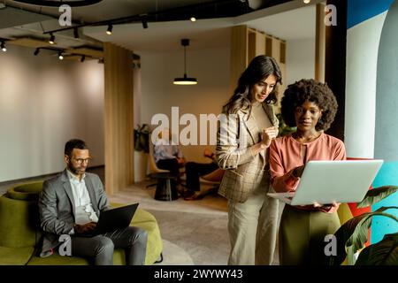 Due professionisti si sono impegnati in una discussione su un notebook, con un collega che lavora in background Foto Stock