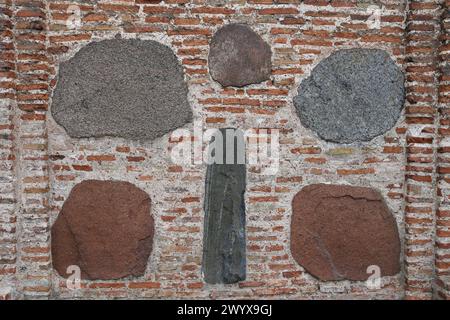 parete in mattoni di mattoni rettangolari di argilla rossa e grandi pietre, ciottoli. Lo sfondo. Foto Stock