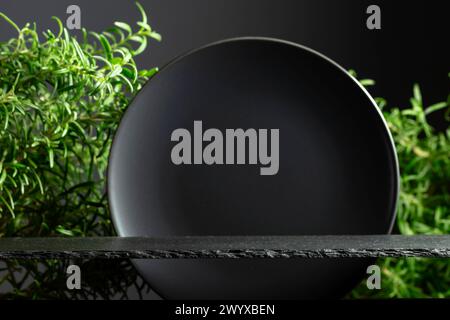 Podio in pietra nera, piastra in ceramica nera e rami di rosmarino per il posizionamento di prodotti di lusso. Eleganza minimalista. Copia spazio. Foto Stock