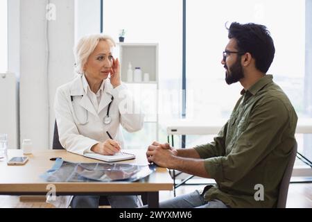 Medico anziano che fornisce consigli utilizzando il notebook per scrivere la prescrizione. Foto Stock