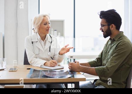 Medico anziano che fornisce consigli utilizzando il notebook per scrivere la prescrizione. Foto Stock