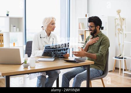 Donna dai capelli grigi con camice da laboratorio che regge la scansione RM. Foto Stock