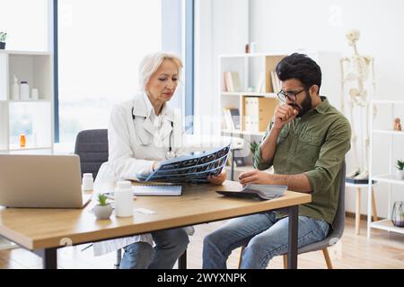 Donna dai capelli grigi con camice da laboratorio che regge la scansione RM. Foto Stock