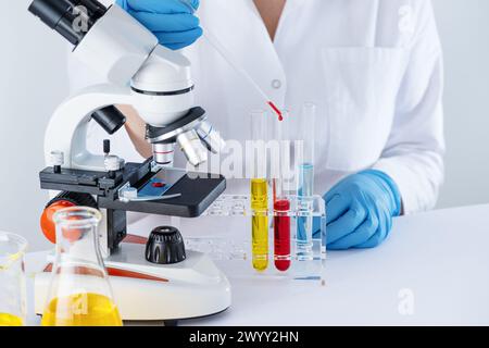 Scienziata biotecnologica donna che lavora in laboratorio con liquido chimico. Lo scienziato sta ricercando in laboratorio, provette per test con liquido e microsco Foto Stock