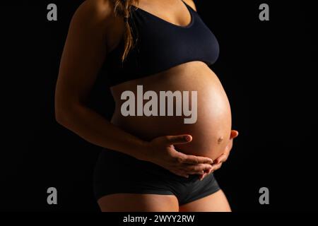 Donna incinta che abbraccia la sua pancia su sfondo nero Foto Stock