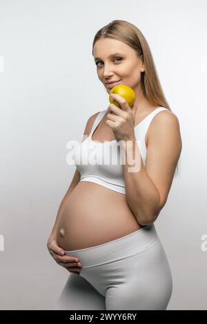 Donna incinta bionda sorridente con mela in mano Foto Stock
