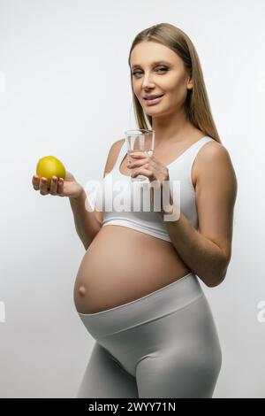 Giovane donna incinta dai capelli lunghi che tiene la frutta tra le mani Foto Stock