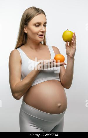 Giovane donna incinta dai capelli lunghi che tiene la frutta tra le mani Foto Stock