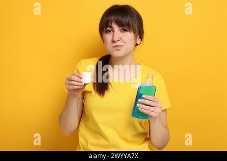 Giovane donna che usa collutorio su sfondo giallo Foto Stock