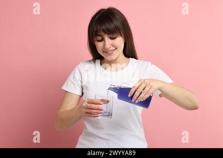 Giovane donna che usa collutorio su sfondo rosa Foto Stock