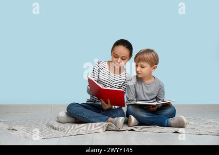 Bambini piccoli che leggono libri seduti sul pavimento vicino al muro blu Foto Stock