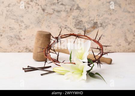 Composizione corona di spine, gigli, unghie e martello su un tavolo bianco vicino alla parete luminosa Foto Stock