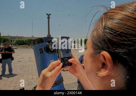 San Juan del Rio, Messico. 8 aprile 2024. Una persona scatta foto all'eclissi solare attraverso un telescopio. Grandi folle si radunano intorno alla piazza principale di San Juan del Rio per assistere a una parziale eclissi del sole durante la grande eclissi solare nordamericana. L'8 aprile 2024, Mazatlan, Messico. (Foto di Fernando Camacho/ credito: Eyepix Group/Alamy Live News Foto Stock