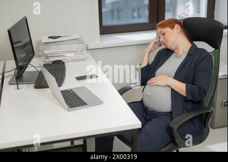 Donna incinta che dorme alla sua scrivania in ufficio. Foto Stock