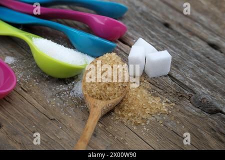 Zucchero di canna di canna di canna e zucchero bianco in colorati misurini di plastica versati su una superficie rustica in legno, misurando utensili in setti da cucina Foto Stock