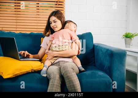 Una madre lavora in modo efficiente dal suo ufficio domestico digitando sul suo laptop mentre sua figlia dorme Foto Stock