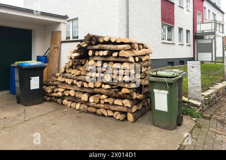 Grande legna da ardere impilata vicino ad un edificio residenziale. I contenitori per rifiuti in plastica si trovano nelle vicinanze. Foto Stock