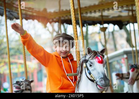 Un ragazzo felice cavalca su un cavallo vintage e gli sventola la mano. Ricordi d'infanzia. Foto Stock