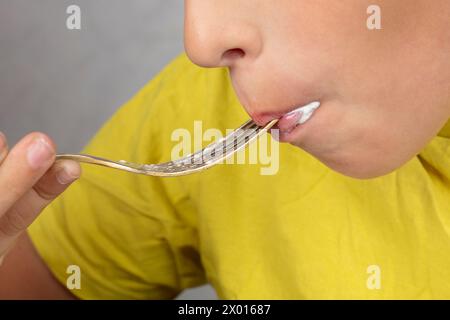 Un bambino, il cui volto non è visibile, tiene una forchetta in bocca. Foto Stock