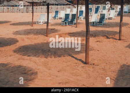 Ombrelloni e sedie a sdraio in paglia di canna sulla spiaggia sabbiosa, concentrazione selettiva Foto Stock