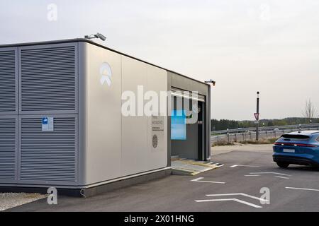 Baviera, Germania - 7 aprile 2024: Stazione di ricarica per auto elettriche NIO Power Swap Station di Nio. Un Nio ET5 entra nella stazione per scambiare la batteria dell'auto elettrica *** NIO Power Swap Station, Ladestation für e-Autos von Nio. Ein Nio ET5 fährt in Die Station um den Akku von dem Elektroauto zu tauschen Foto Stock