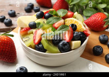 Gustosa Macedonia di frutta nel recipiente e ingredienti su un tavolo di legno, primo piano Foto Stock