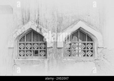Un'immagine monocromatica, filtrata e vignettata di due finestre ad arco con reticoli di legno nel muro di un edificio abbandonato e abbandonato nel Middl Foto Stock