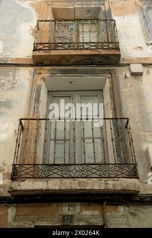 Un primo piano di un antico balcone con ringhiere ornate su un vecchio edificio urbano con pareti in angoscia Foto Stock