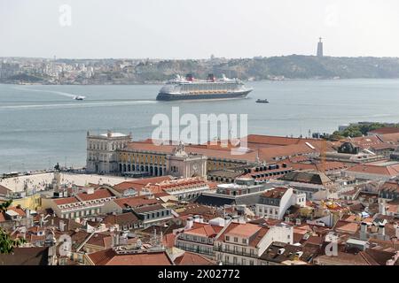 Una nave della Disney Cruise Lines nelle vendite a distanza sul fiume Tago a Lisbona, in Portogallo, con la Prac do Comércio (piazza del commercio) in primo piano. Foto Stock