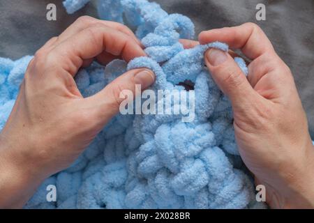 Una donna crea amorevolmente una coperta blu per suo nipote con le proprie mani, ciascuna delle quali costituisce una testimonianza della sua cura e devozione. Creare memorie preziose Foto Stock