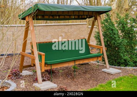 Altalena da giardino in legno con materasso verde e una lunga seduta sotto il tetto Foto Stock