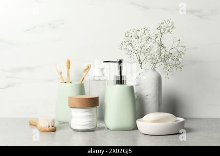 Diversi accessori per il bagno, prodotti per la cura personale e fiori di gypsophila in vaso su tavolo grigio vicino alle pareti in marmo bianco Foto Stock