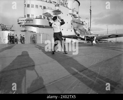 BRACCIO AEREO DELLA FLOTTA. 7 GENNAIO 1942, A BORDO DELLA HMS VICTORIOUS. PILOTI DI CACCIA E LE LORO MACCHINE. - Abbattere un aereo. L'ufficiale di parcheggio nel ponte di volo della HMS VICTORIOUS che ha segnalato un Fairey Fulmar all'ascensore prima di essere abbattuto Foto Stock